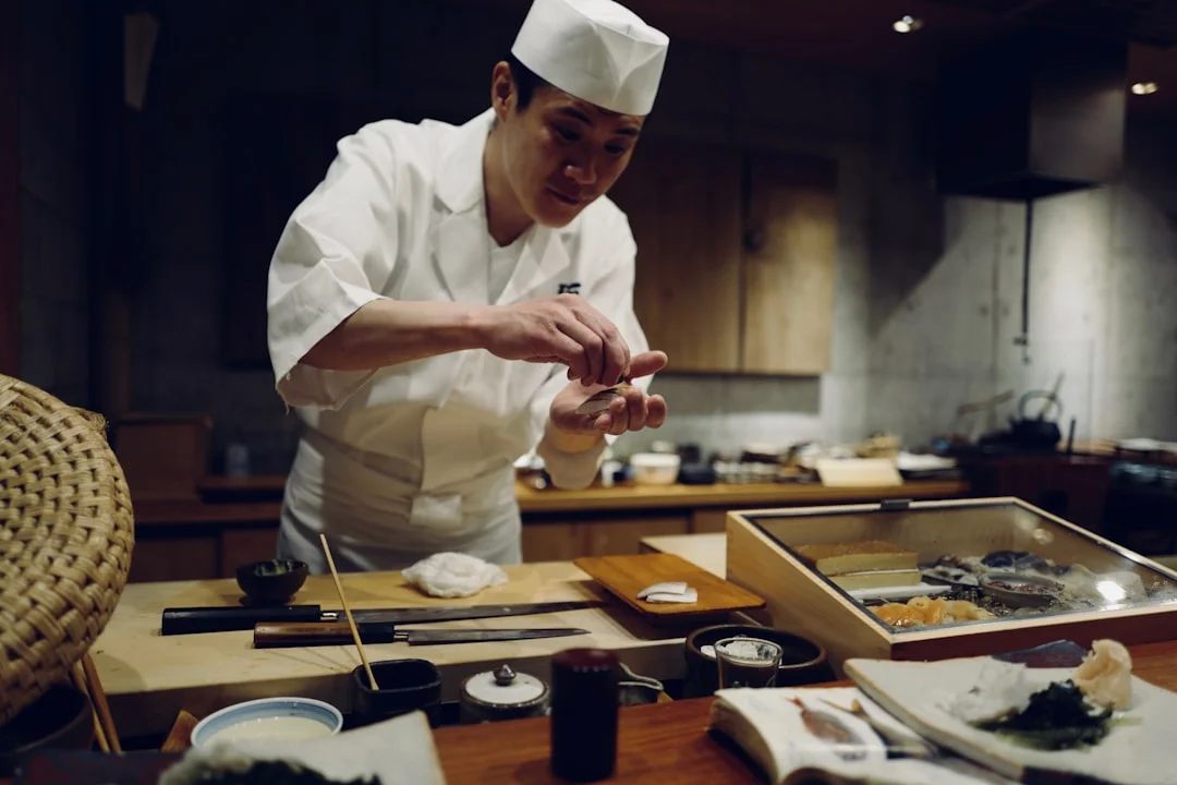 A hand-forged Japanese gyuto knife resting beside a rustic donabe clay pot and a set of hand-thrown Arita porcelain bowls on a dark wooden kitchen counter